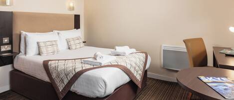 A hotel room with a neatly made bed, a desk with a chair, and a wall-mounted TV.