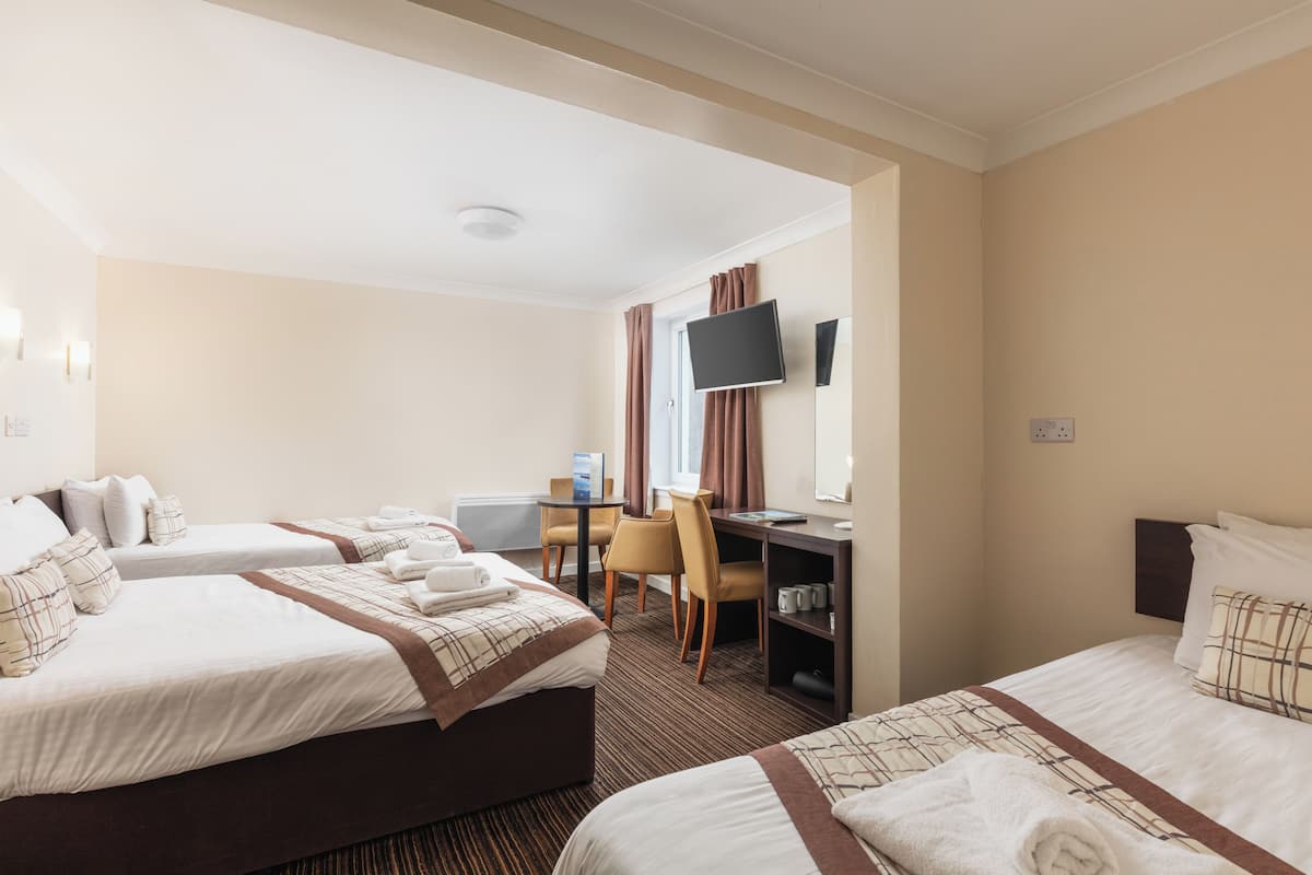 A hotel room with two beds, a desk, a chair, a television, and a small table with a cup and a book.