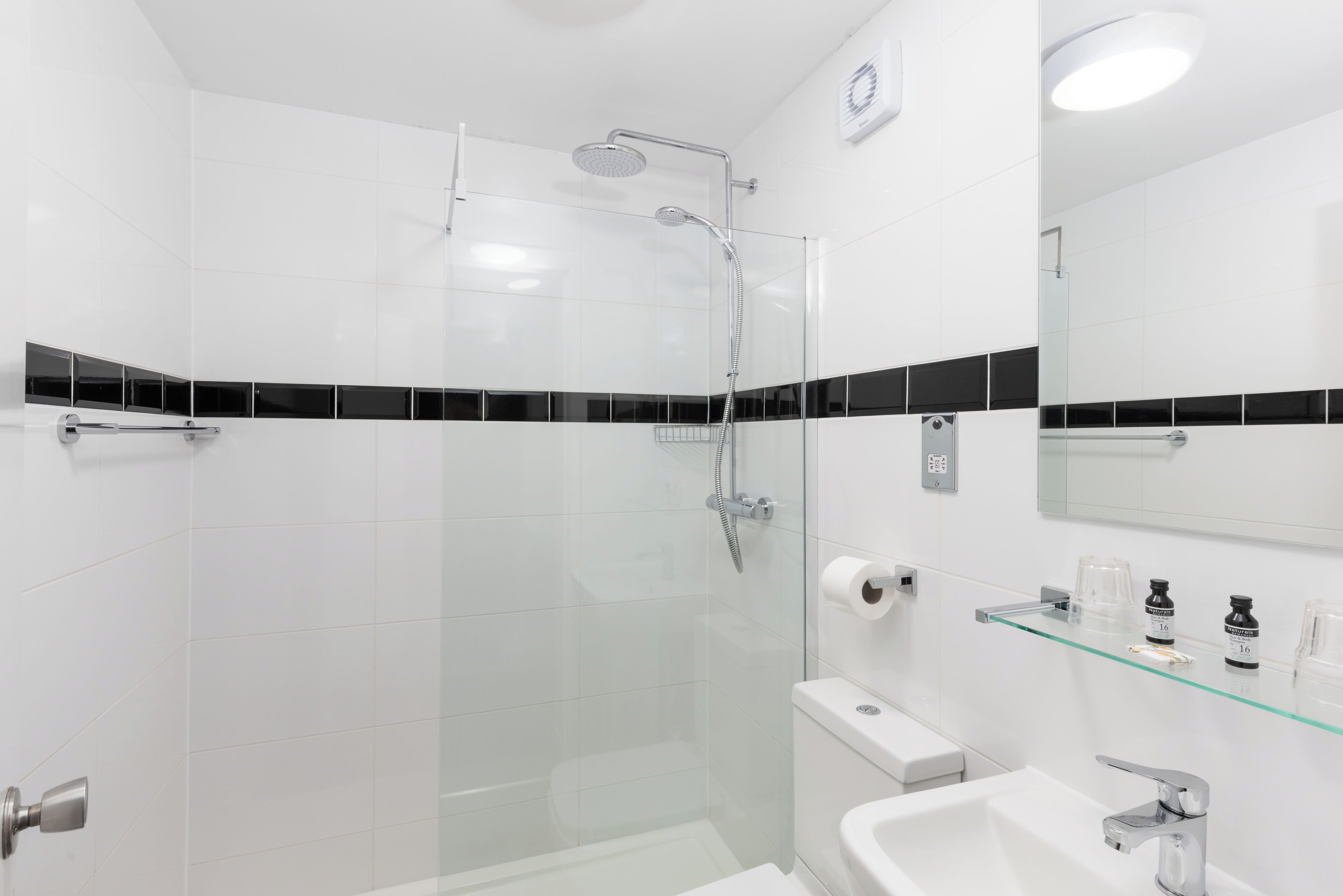 Une salle de bain moderne avec une douche à parois de verre, un lavabo blanc et une étagère en verre où sont rangés les articles de toilette.