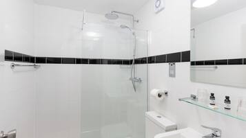 A modern bathroom with a glass-enclosed shower, a white sink, and a glass shelf with toiletries.