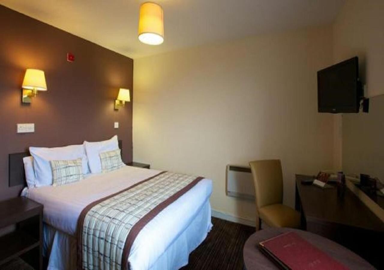 A hotel room with a bed, bedside tables, a chair, a desk, and a TV.