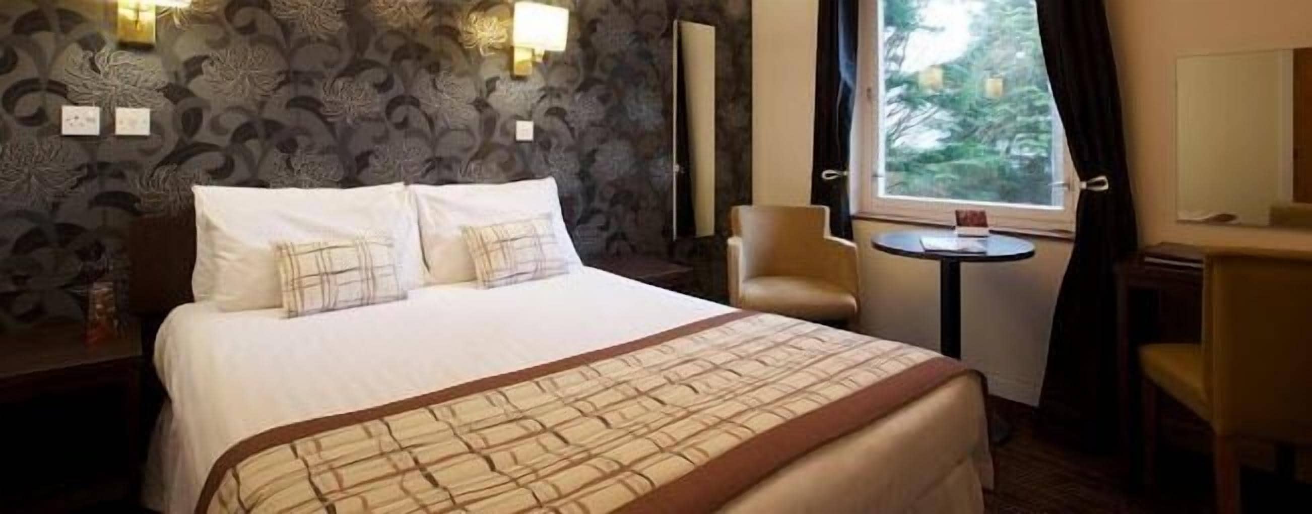 Una camera d'albergo con un letto grande, un tavolino rotondo, una sedia e una finestra con tende.