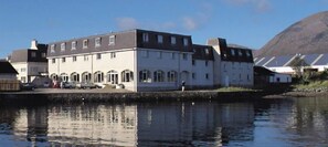 A large, multi-story building with a symmetrical facade, a flat roof, and a reflective water body in front. - Dunollie Hotel (Strath)