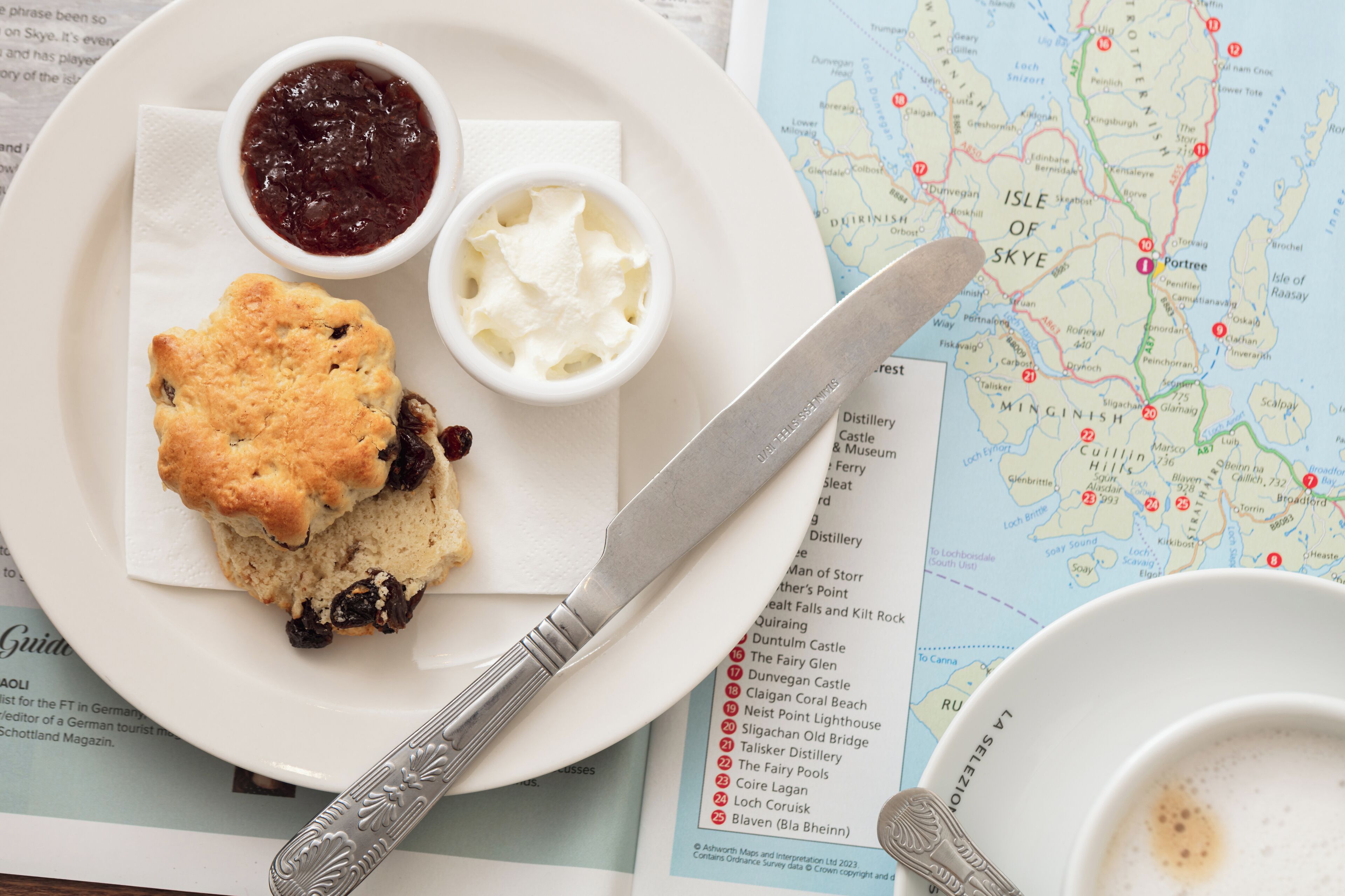 Une assiette avec des scones, de la confiture et de la crème, un couteau et une carte, ainsi qu’une cuillère.