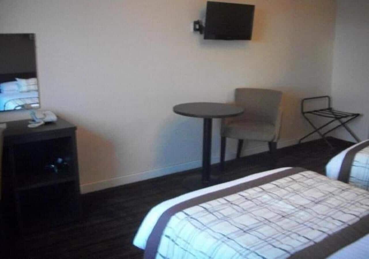 Habitación de hotel con cama, escritorio, silla y televisor montado en la pared.