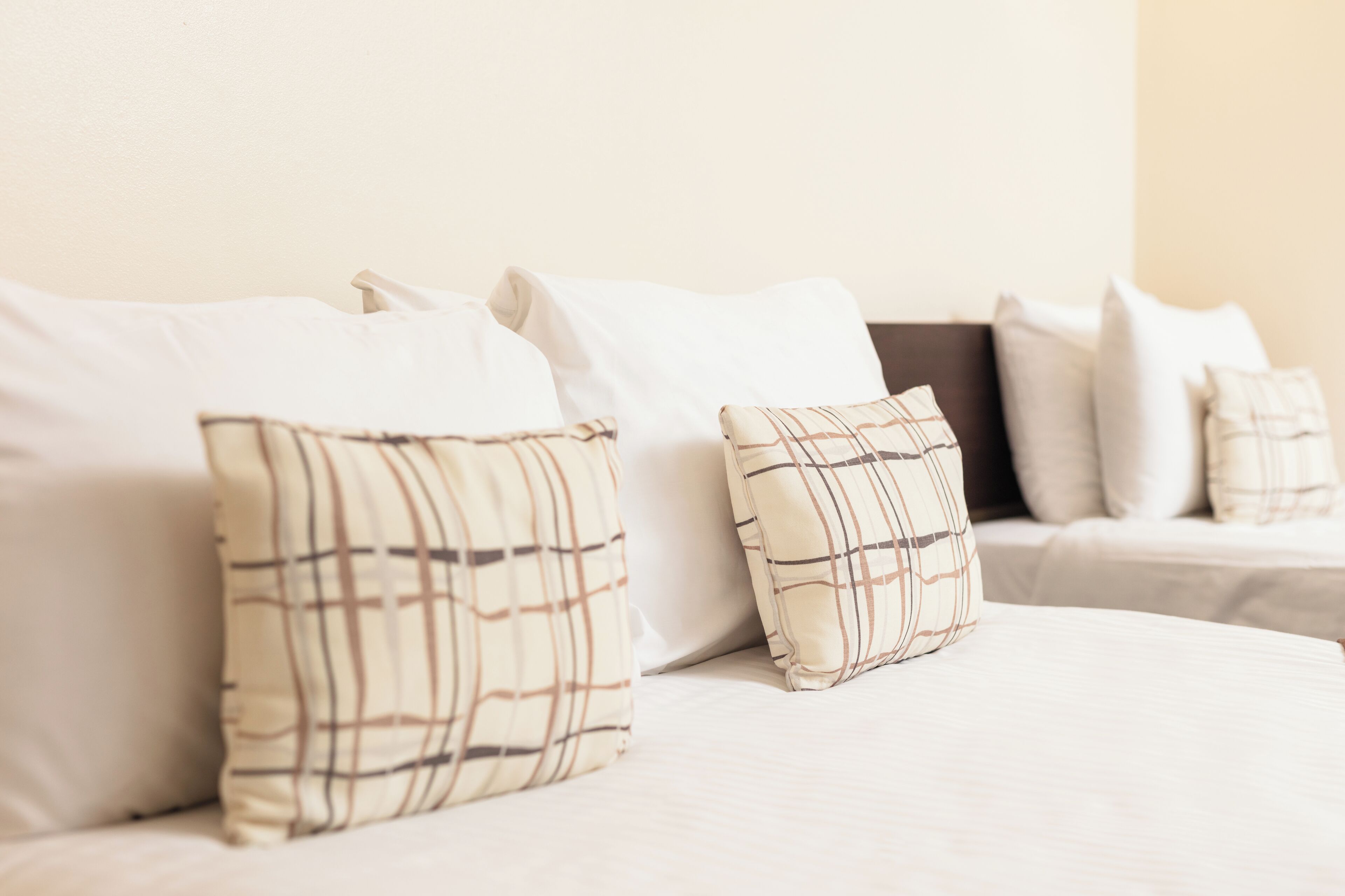 A bed with white bedding and two plaid pillows.