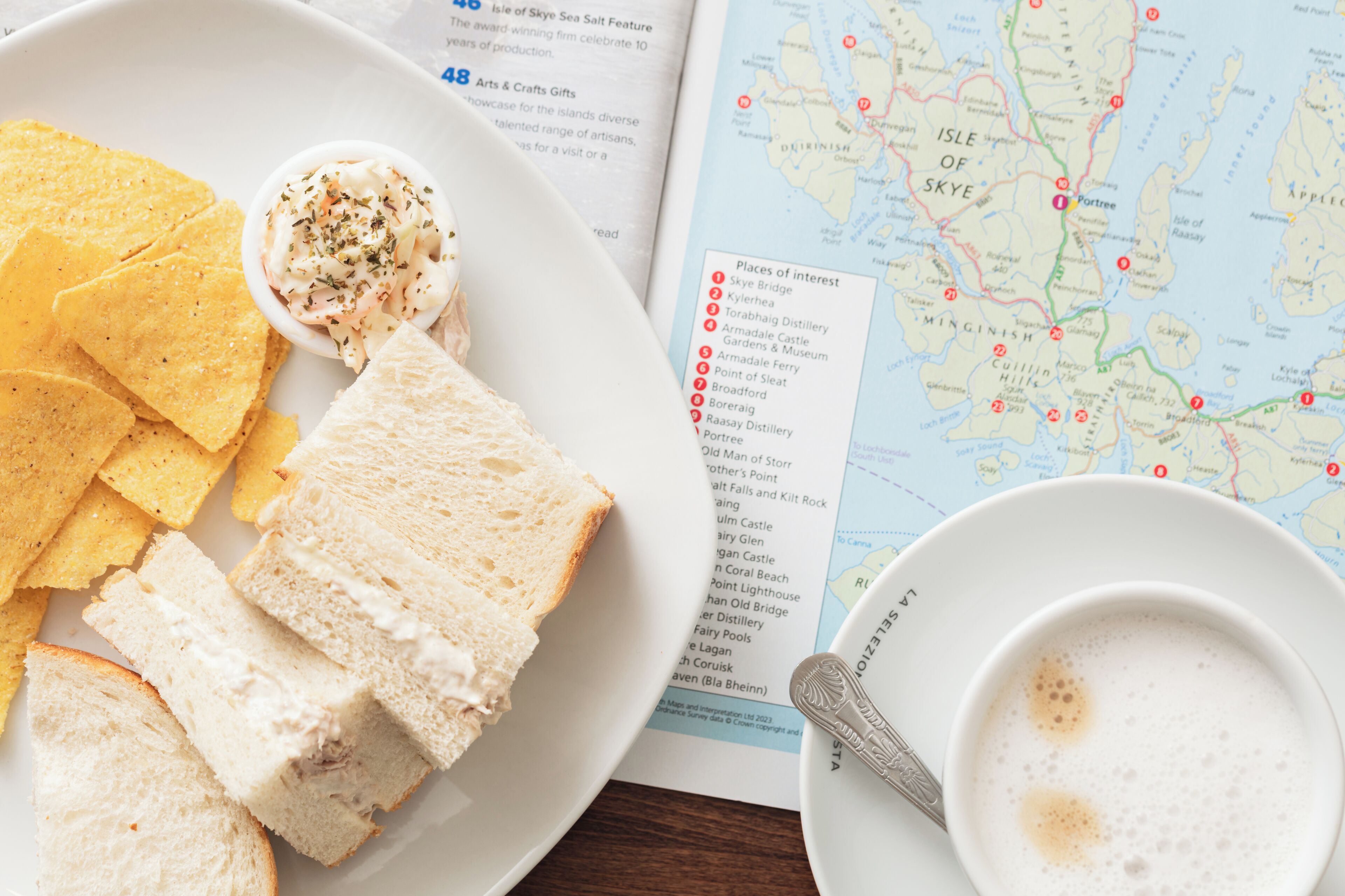 A plate with slices of white bread, a small bowl of salad, and yellow chips. A cup of coffee with a spoon is also visible.