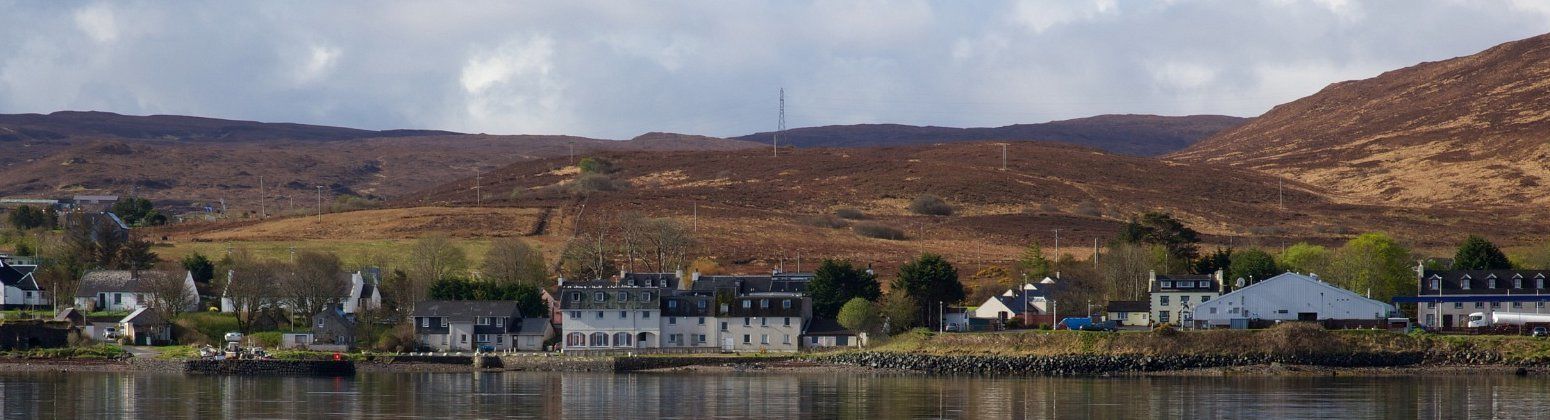 A coastal town with buildings along the shoreline, a body of water, and hills in the background.