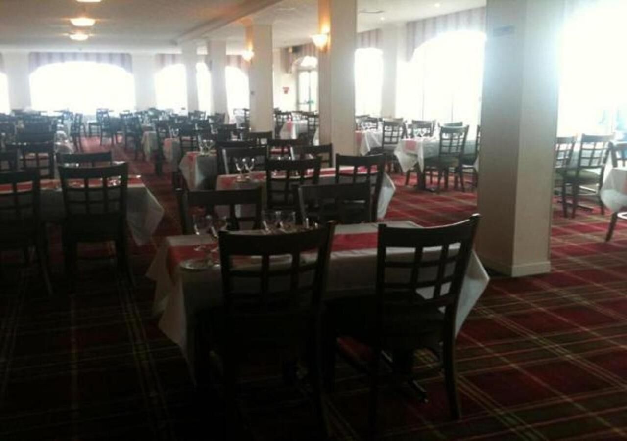 A large dining hall with multiple tables and chairs, carpeted floor, and large windows.