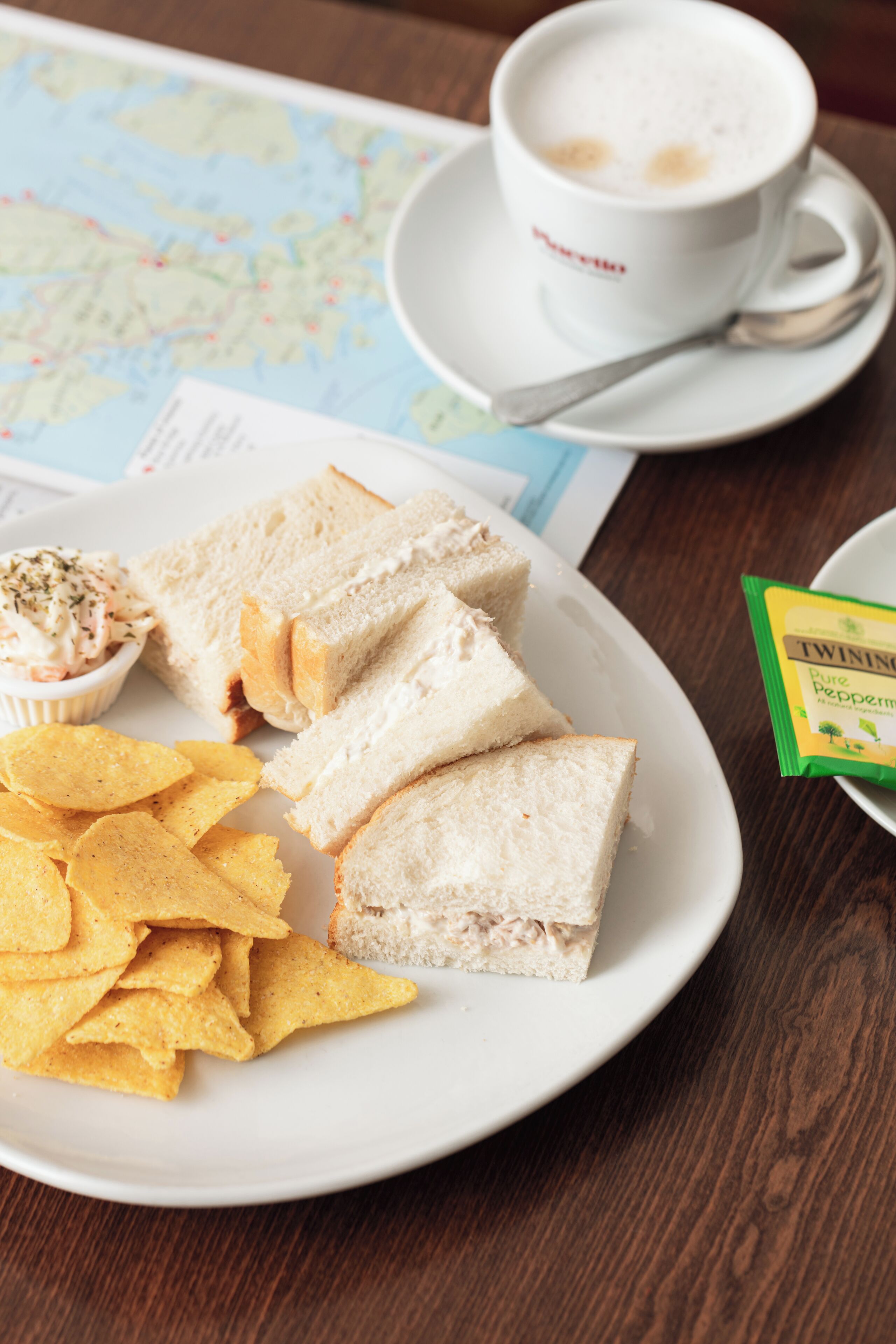 A plate with sandwich slices, chips, and a cup of coffee on a table with a map.