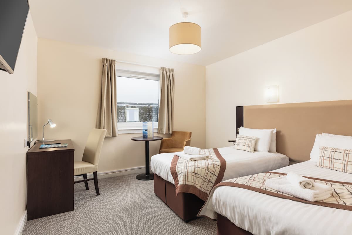 A hotel room with two beds, a desk, a chair, a small table, and a window with curtains.