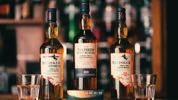 Tres botellas de whisky escocés Talisker de malta única y dos vasos para chupito sobre una barra.