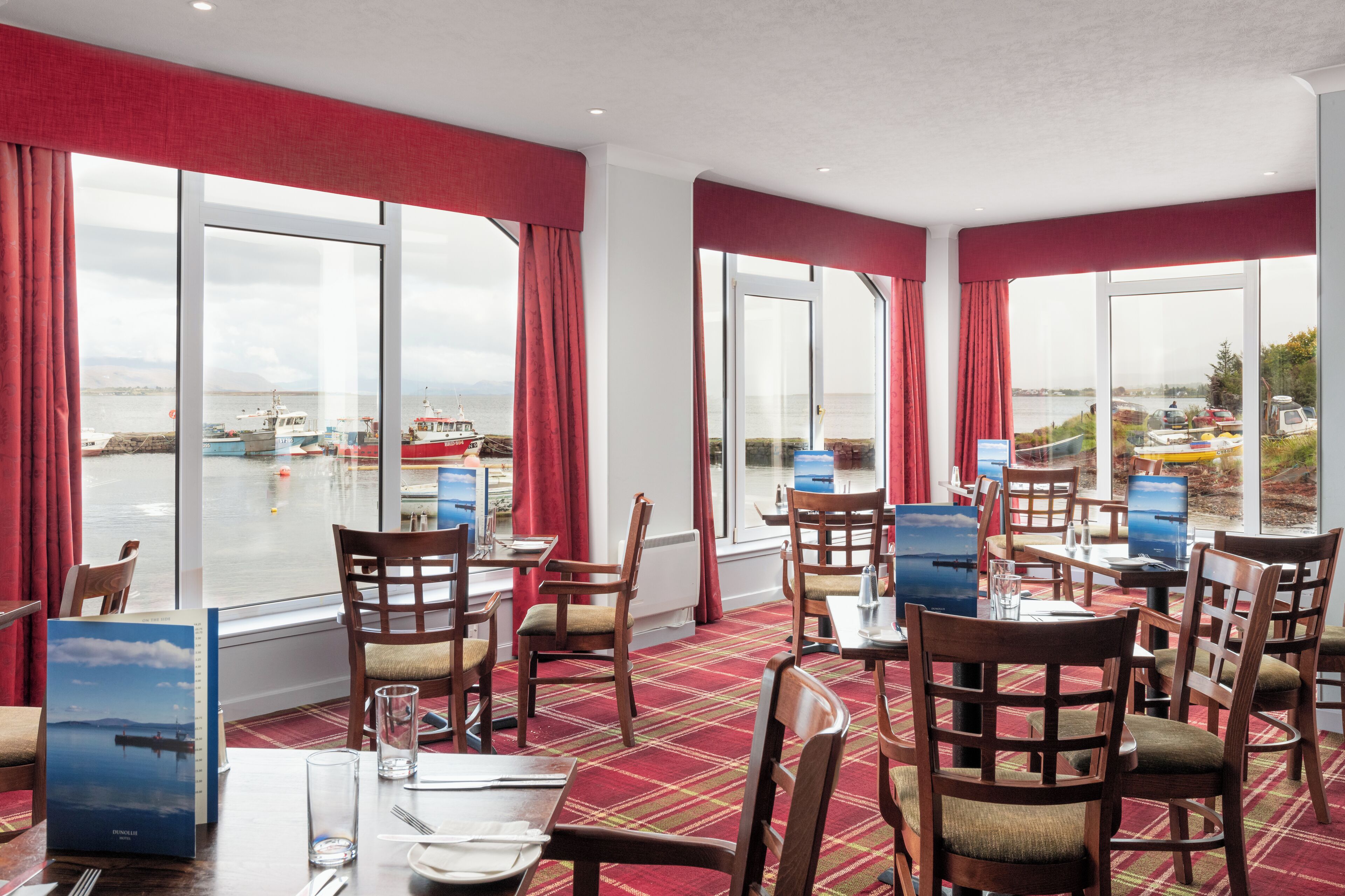 A restaurant with large windows, wooden chairs, and a red carpeted floor.