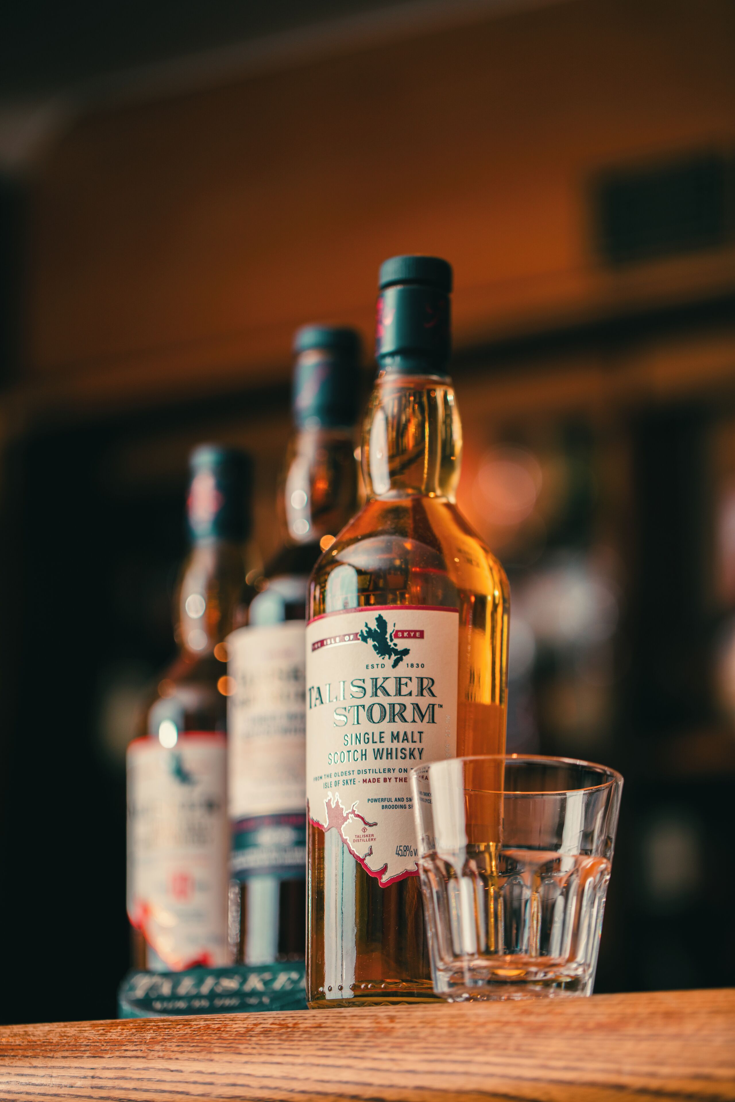 A bottle of whisky with a label, a glass, and other bottles in the background.