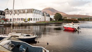 A waterfront building with a docked boat, a sailboat, and a mountain in the background. - Dunollie Hotel (Strath)