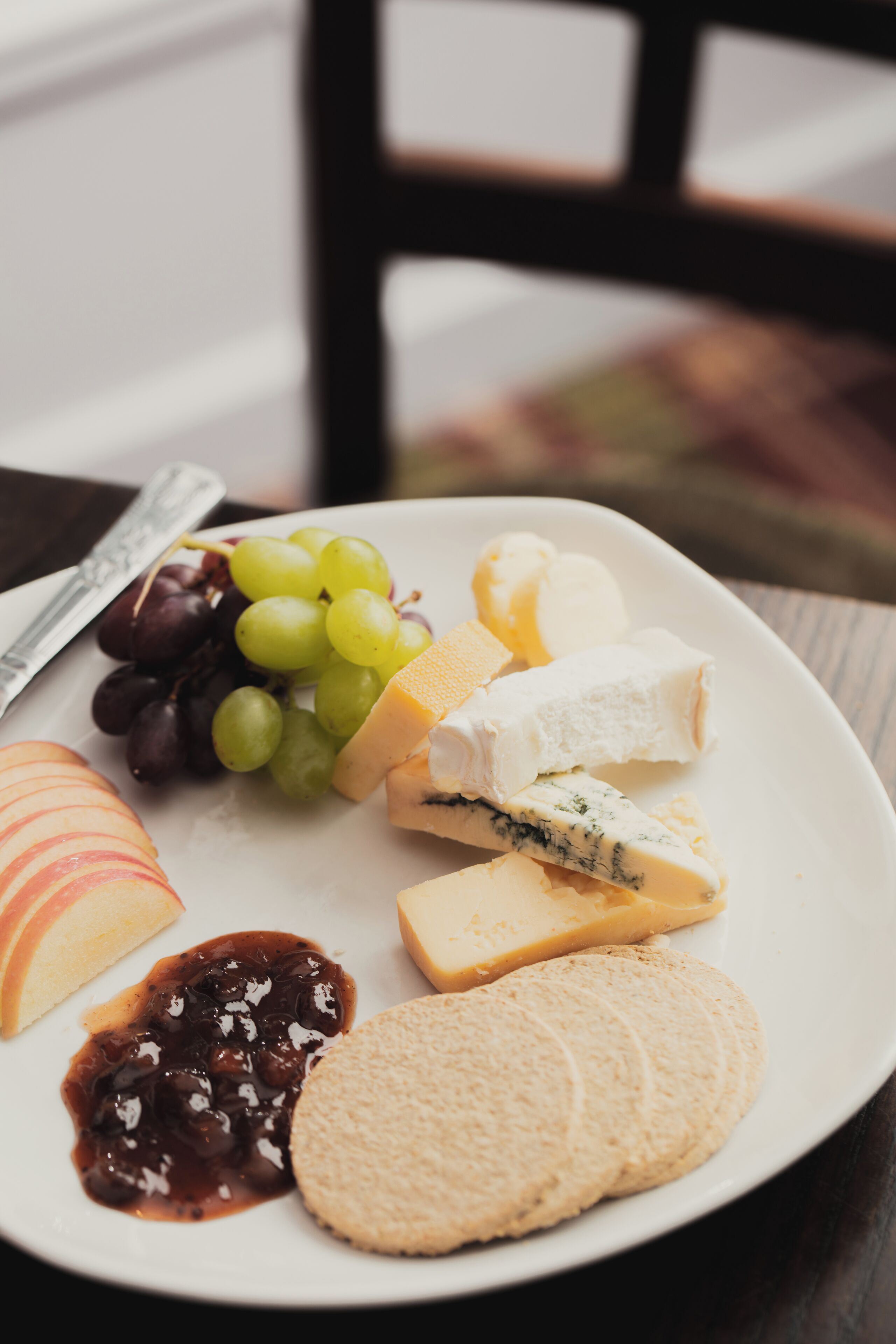 A plate with various cheeses, grapes, apple slices, and crackers.