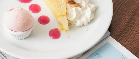 Un plato con una porción de pastel, crema batida y una bola de helado sobre una mesa junto a un libro abierto.