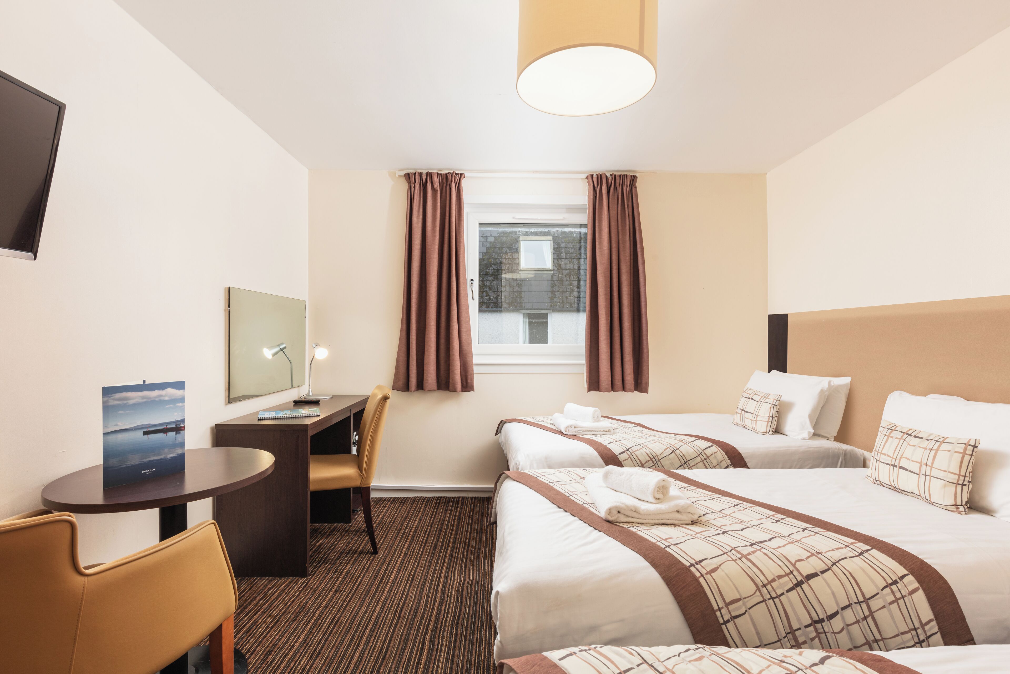 A hotel room with two beds, a desk, a chair, a television, and a window with curtains.