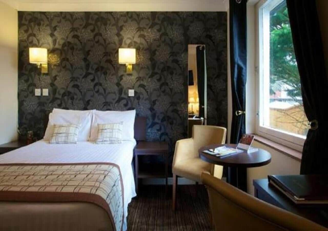 A hotel room with a bed, a chair, a table, and a window with curtains.