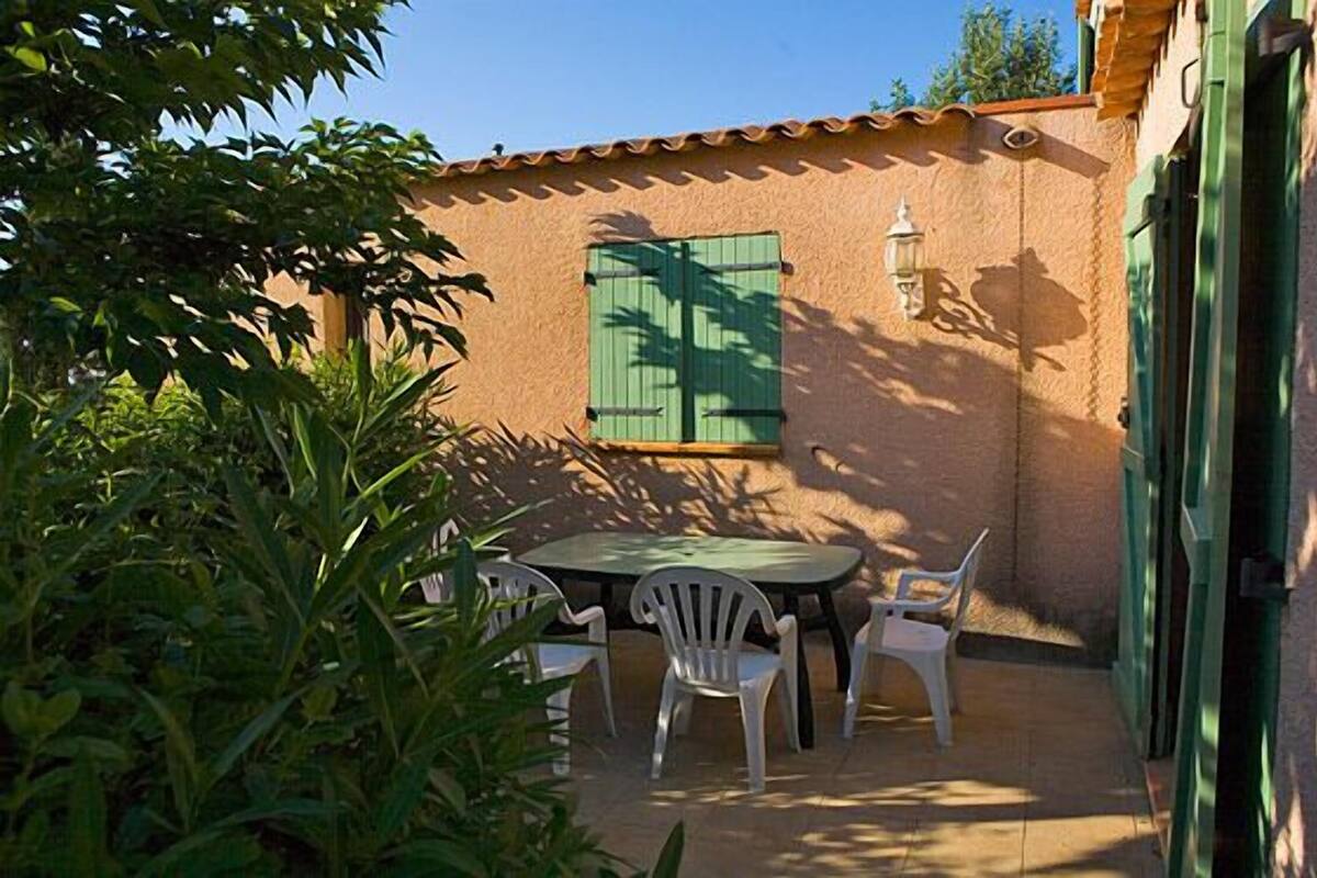 Un patio con una mesa redonda y sillas blancas, rodeado de follaje.
