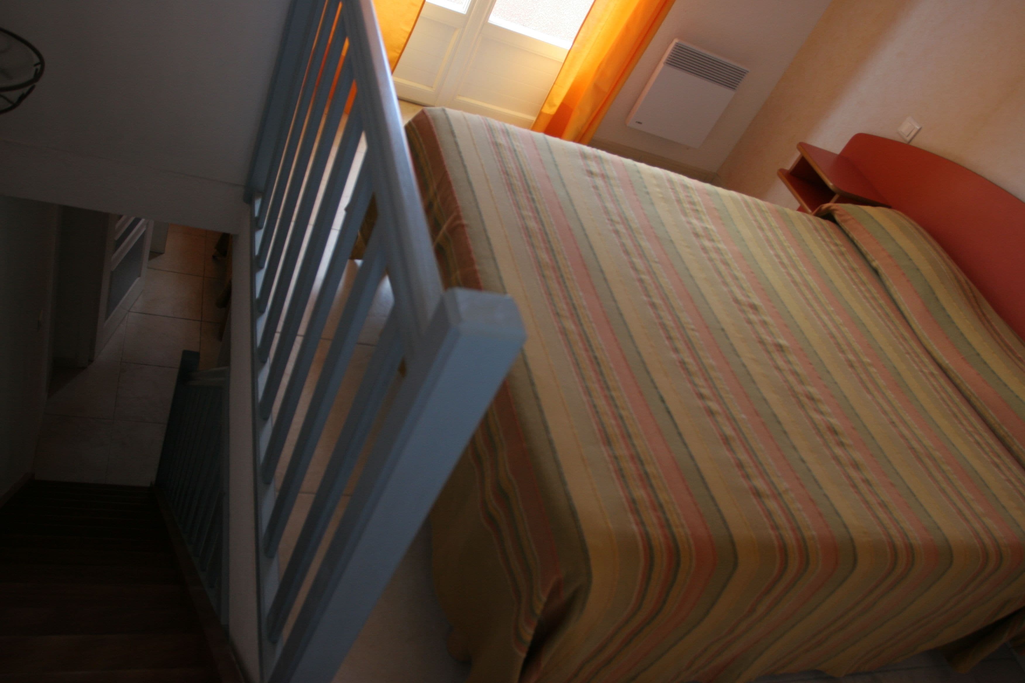 Une pièce avec un lit, une fenêtre avec des rideaux, un radiateur et un escalier.