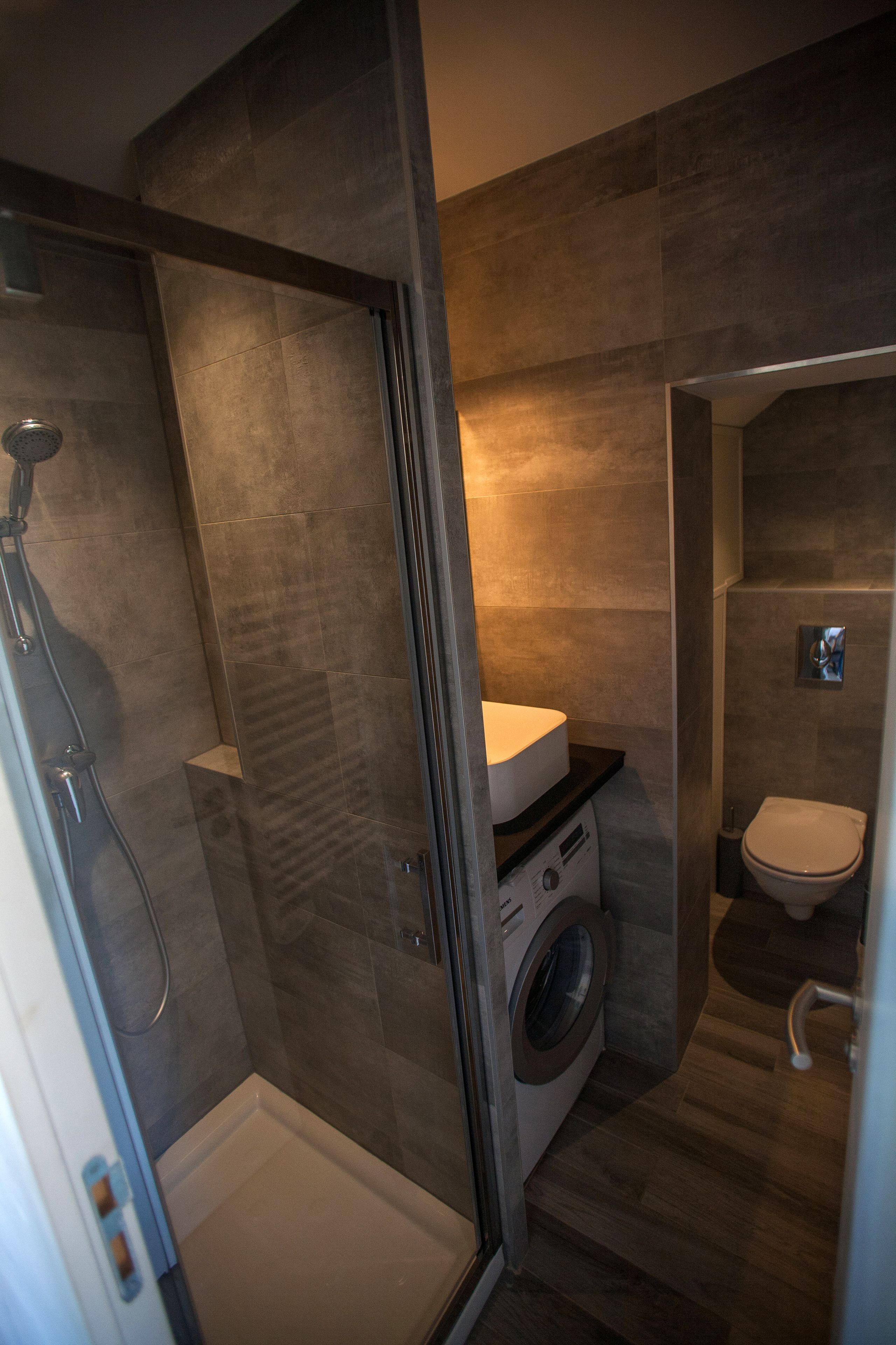 A compact bathroom with a glass-enclosed shower, a built-in washing machine, and a toilet.
