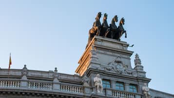 Un edificio con una llamativa escultura de cuatro caballos en la parte superior, detalles arquitectónicos elaborados y un asta de banderas.