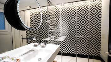 Un baño moderno con un revestimiento mural de diseño geométrico, un lavamanos blanco con espejo y una zona de ducha.