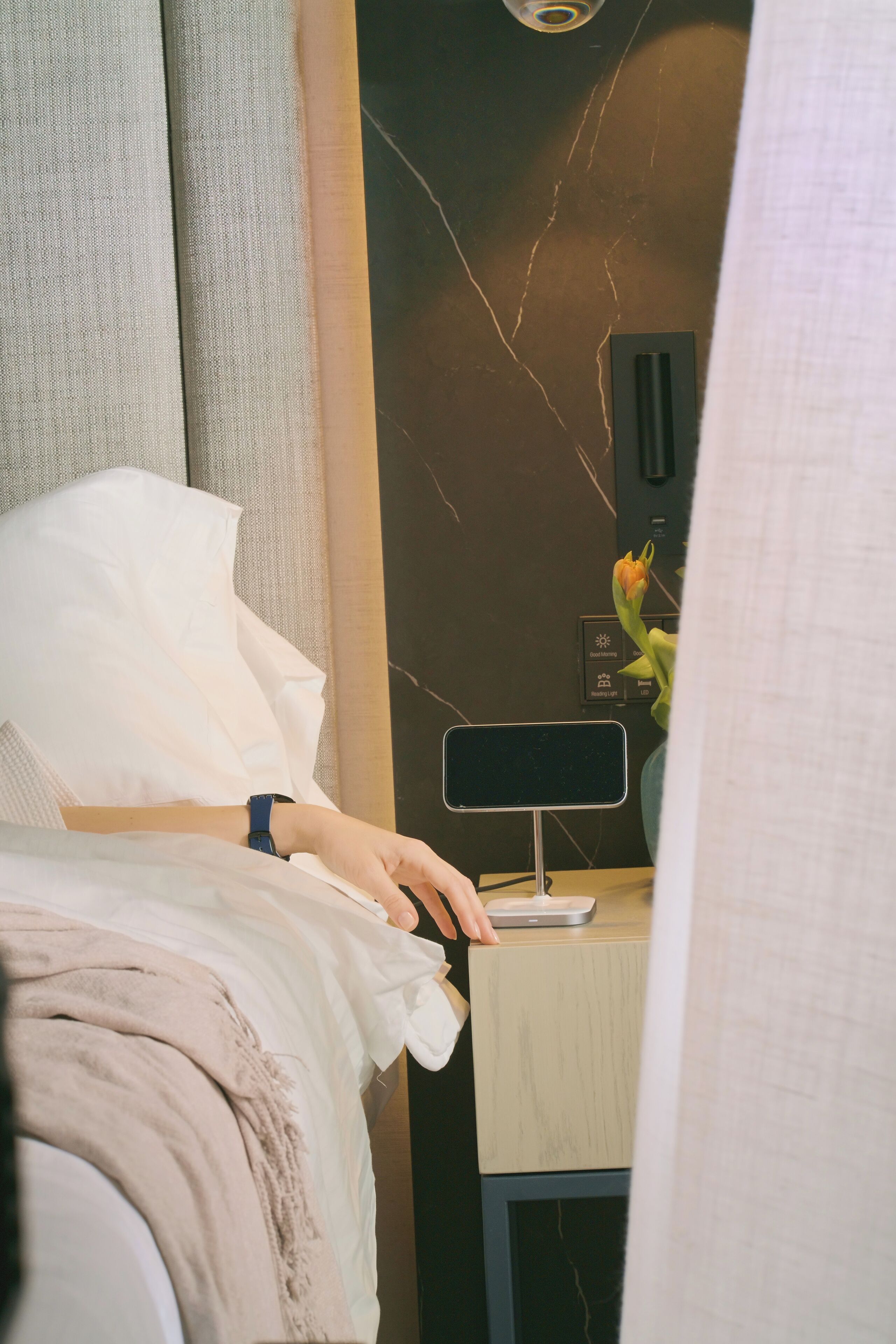 A hotel room with a bed, a bedside table with a lamp, and a wall-mounted air purifier.