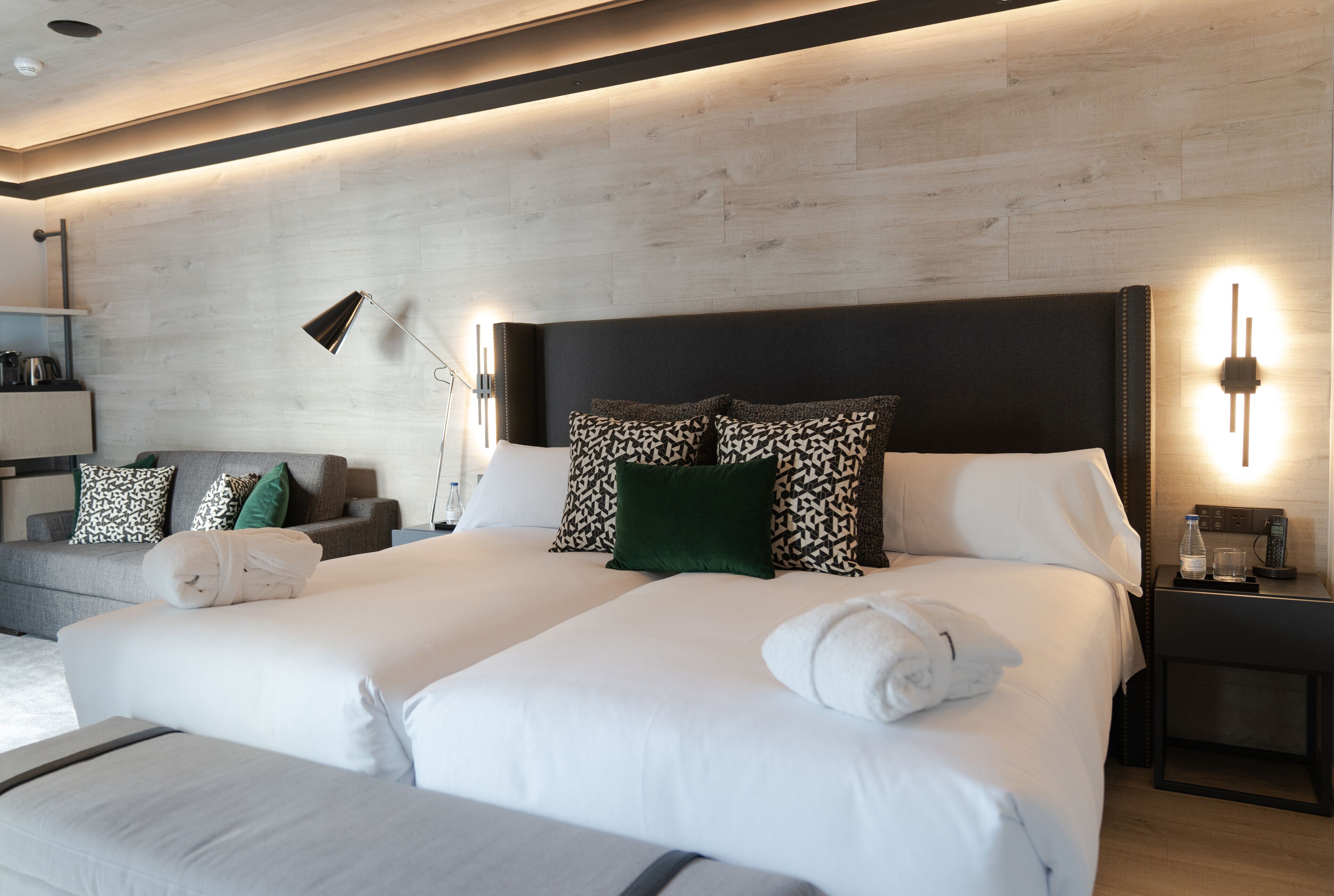 A modern hotel room with a large bed, a bedside table with a lamp, and a wall-mounted light fixture.
