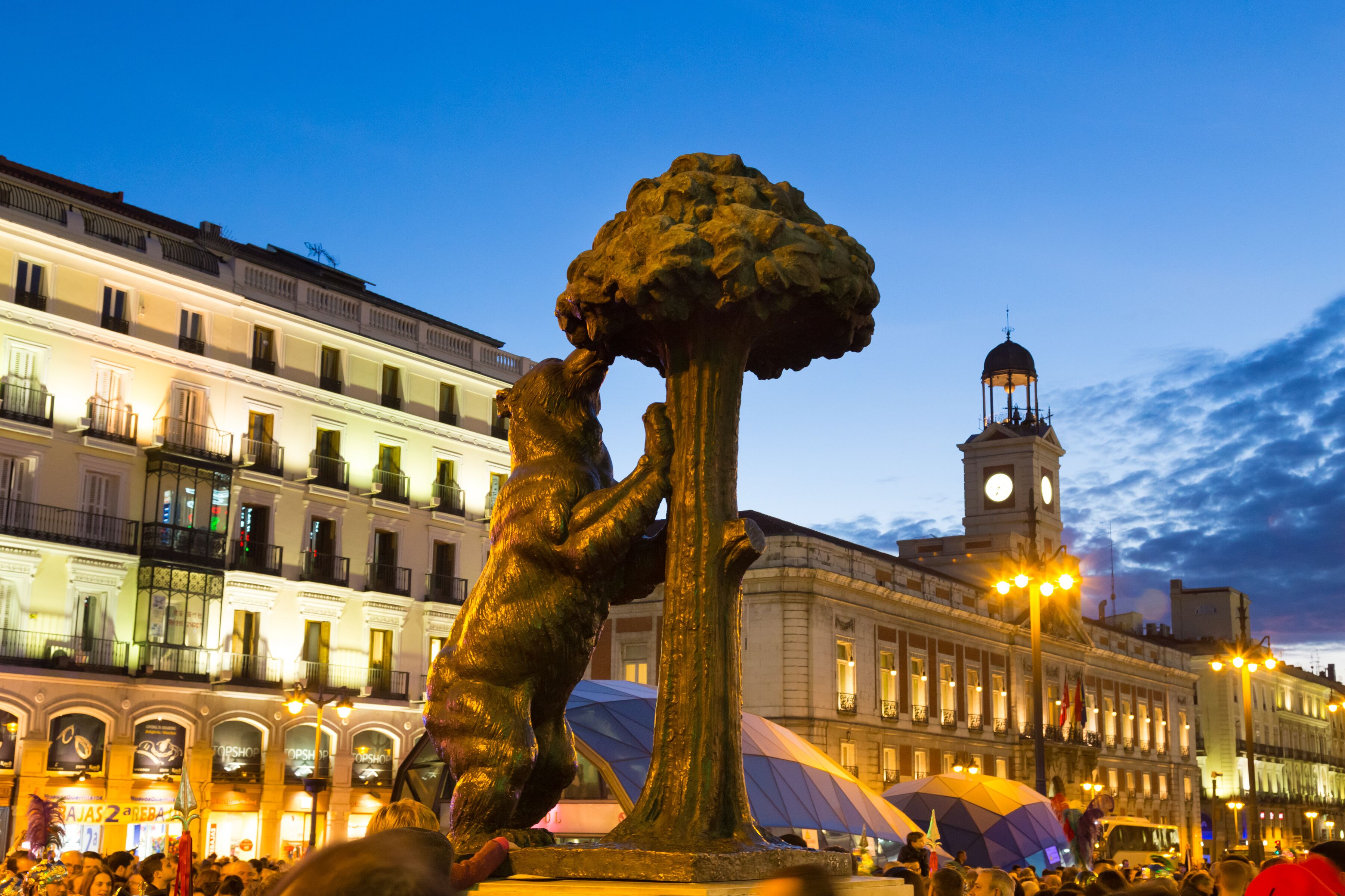 A public square with a prominent statue, historic buildings, and a clock tower.