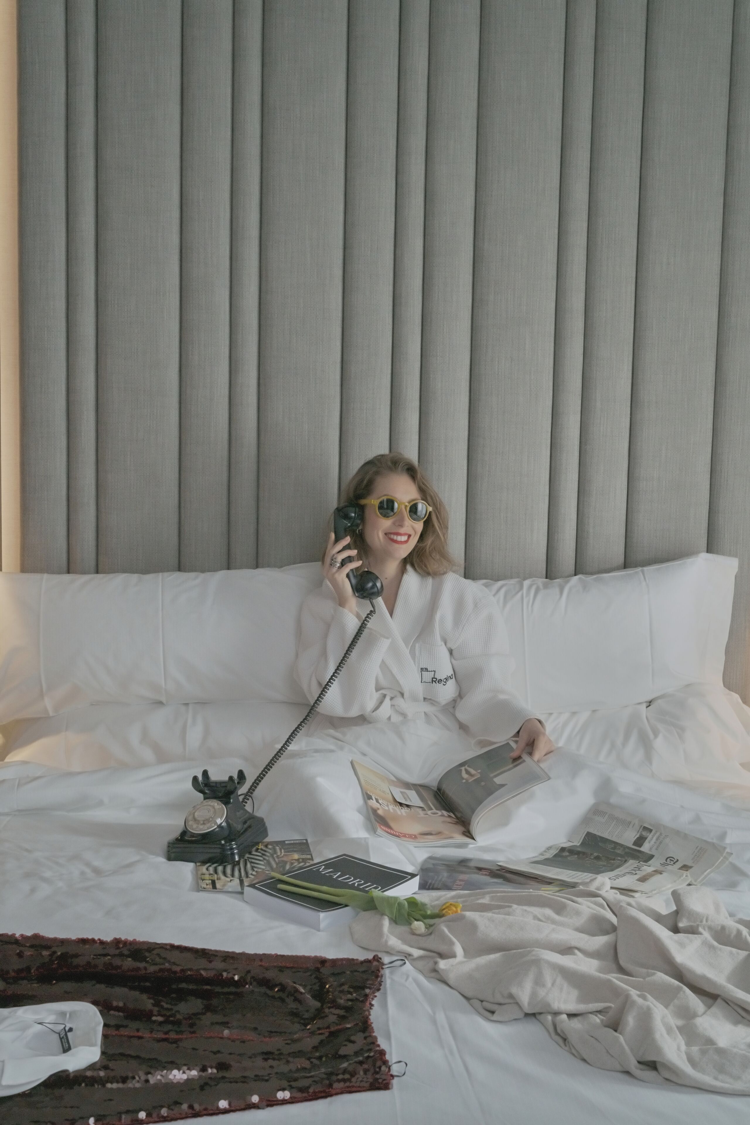 Une personne assise sur un lit, avec un téléphone, un livre et une télécommande.