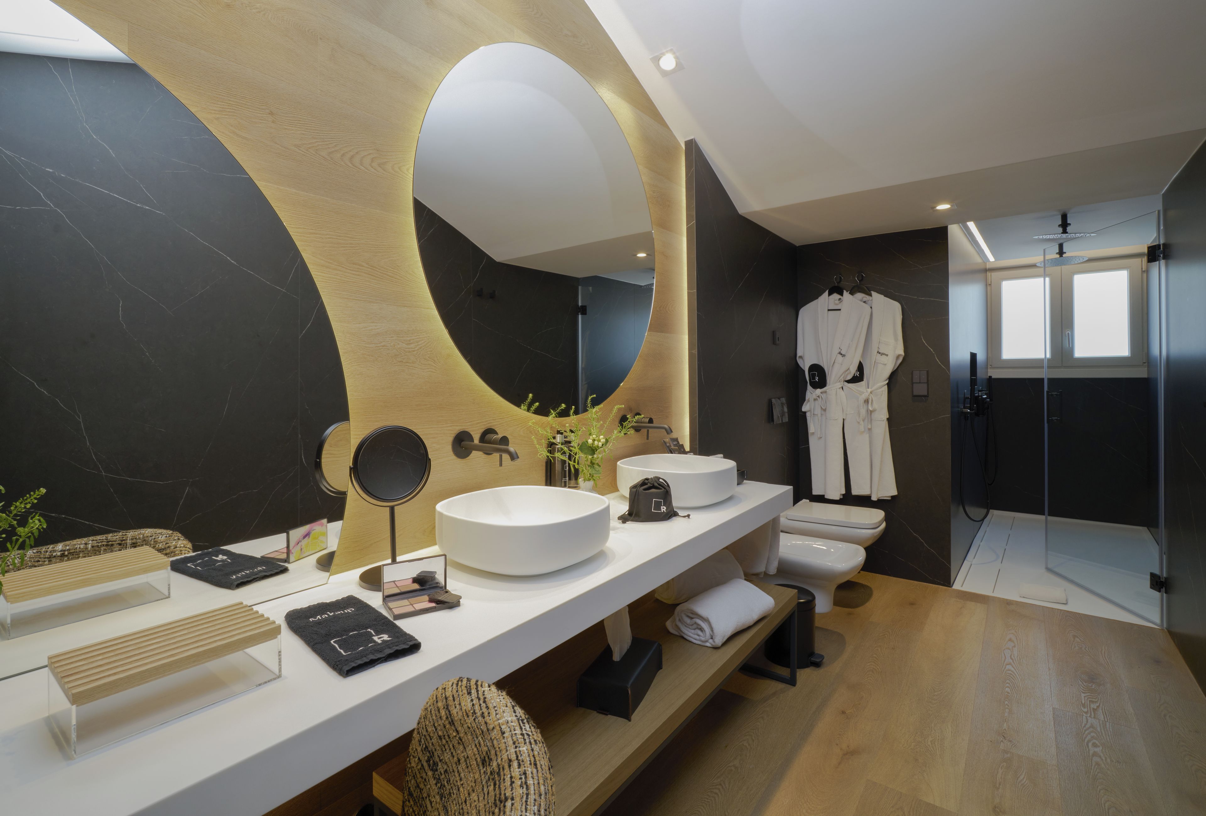 A modern bathroom with a large mirror, a round sink, and a walk-in shower.
