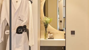 A modern bathroom with a large mirror, a robe hanging on a rack, and a towel shelf. - Hotel Regina (Madrid)