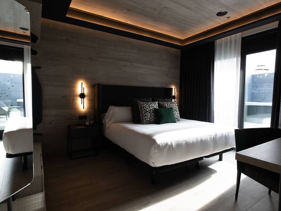 Una habitación de hotel moderna con una cama grande, mesitas de noche, un escritorio y vistas a la ciudad.