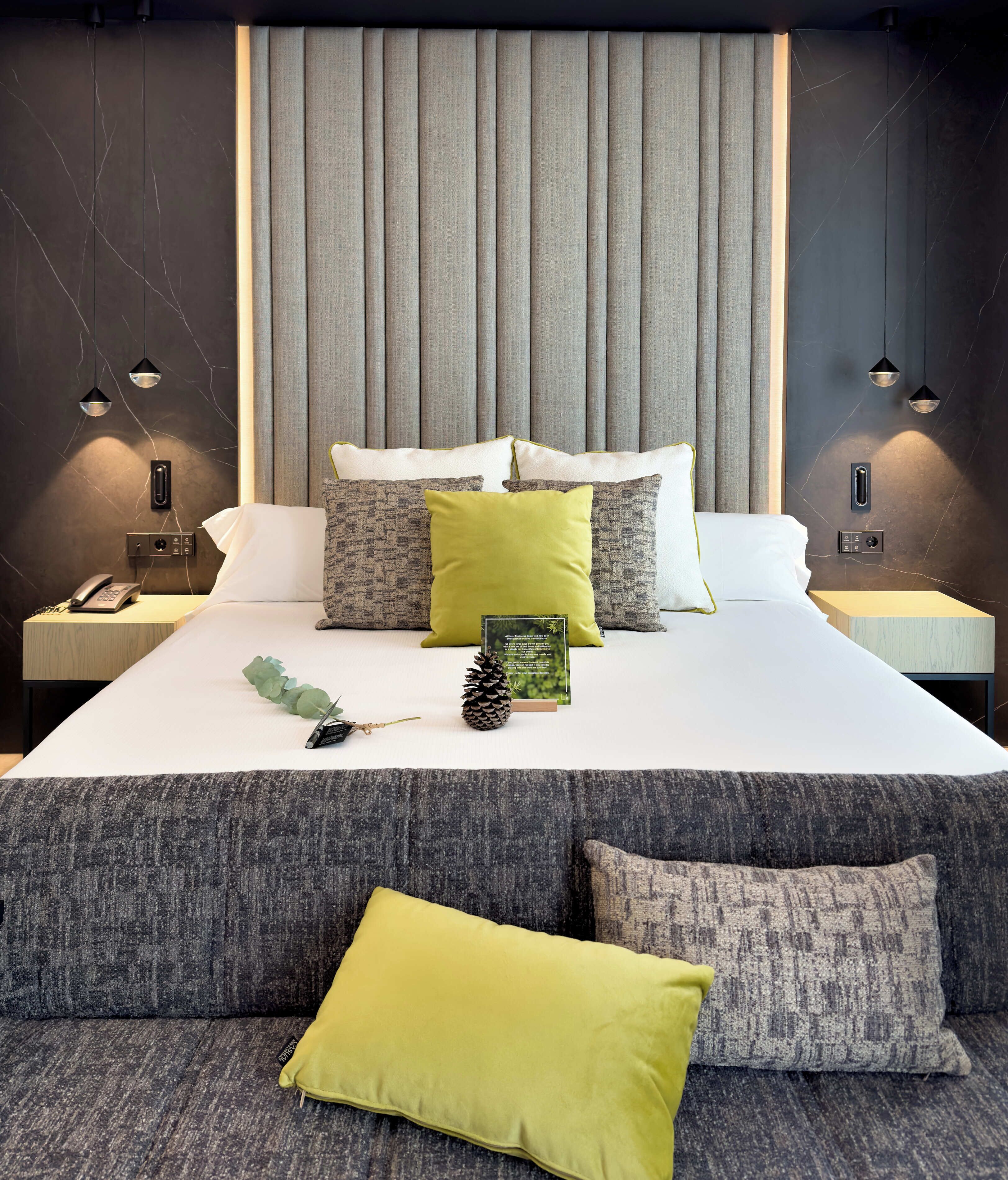 Una habitación de hotel moderna con una cama grande, cabecero tapizado en gris y mesitas de noche a juego.