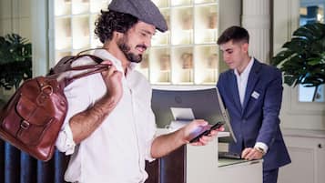 A man in a white shirt and brown pants standing at a reception desk, holding a smartphone.