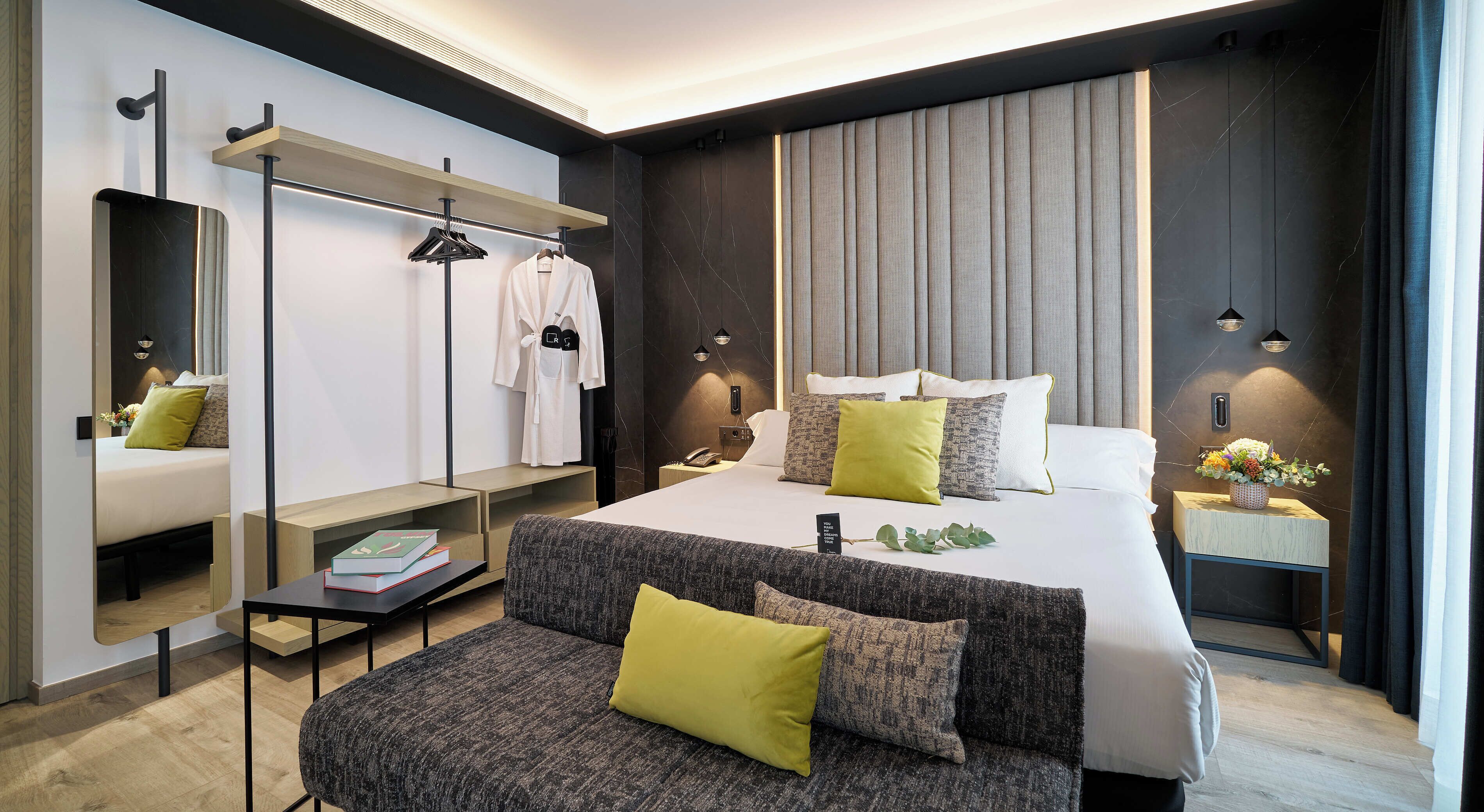 Ein modernes Hotelzimmer mit einem großen Bett, einer Sitzecke, einem Schminktisch mit Spiegel und einem Kleiderschrank.