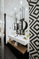 Ein modernes Badezimmer mit einem weißen Waschtisch, zwei Spiegeln und einer Wand mit geometrischem Muster.