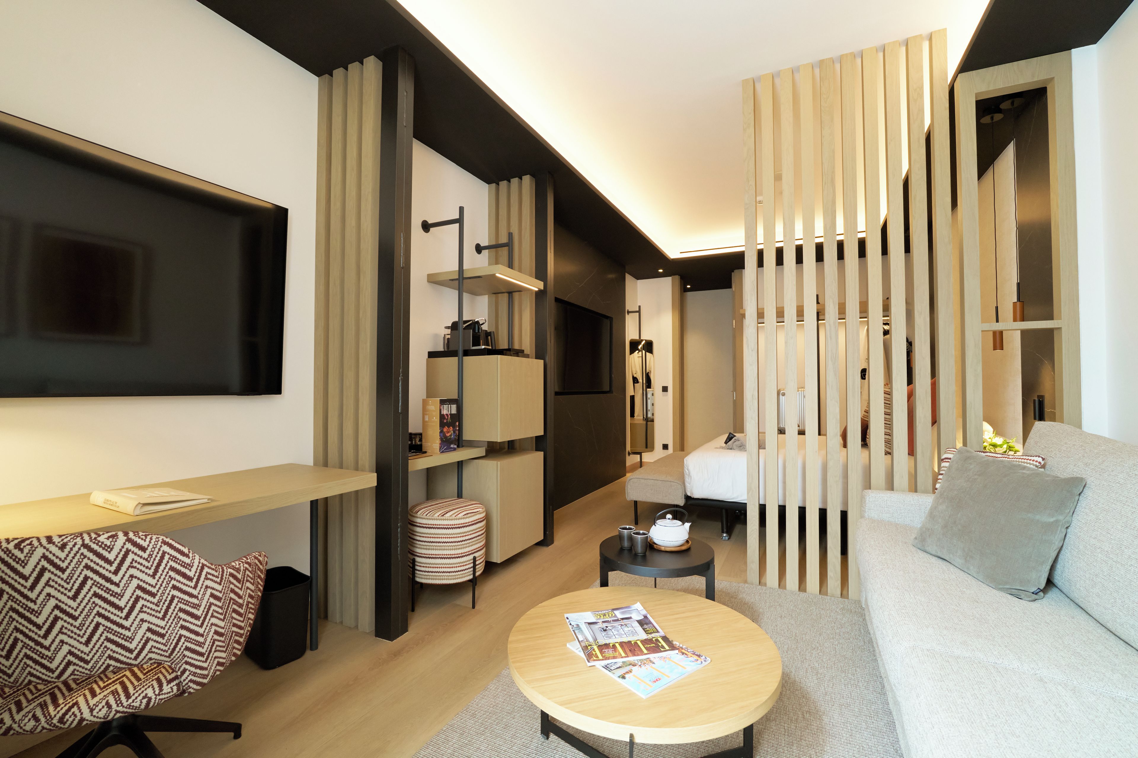 A modern living room with a flat-screen TV, a round coffee table, a sofa, a bookshelf, and a sliding door separating the living area from a bedroom.