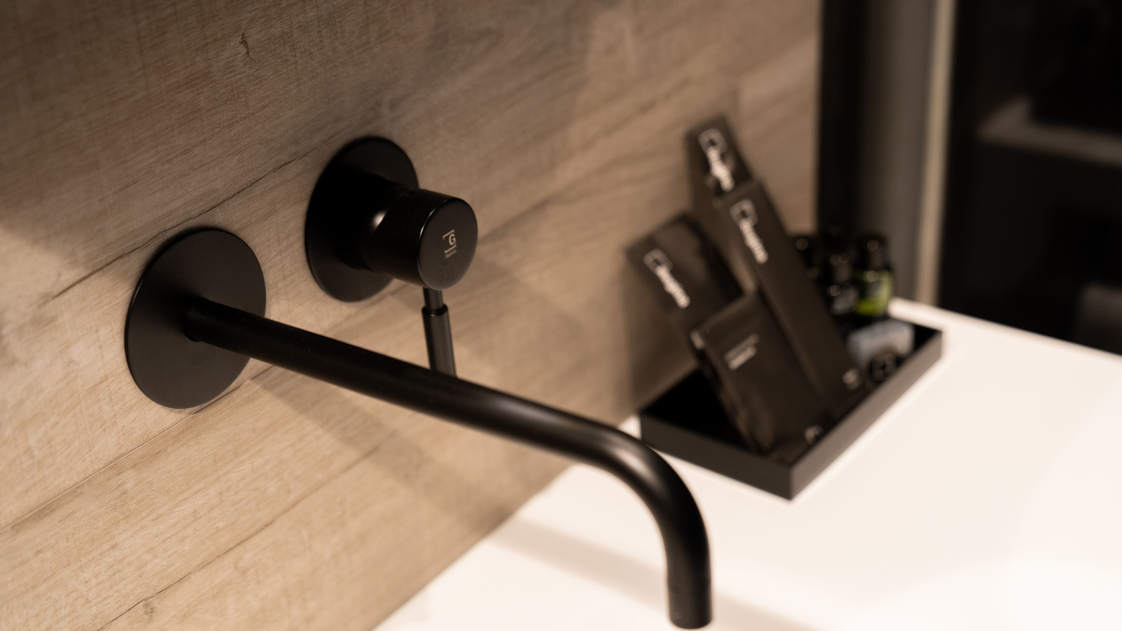 Un baño moderno con pared de madera, grifo negro y toallero negro.