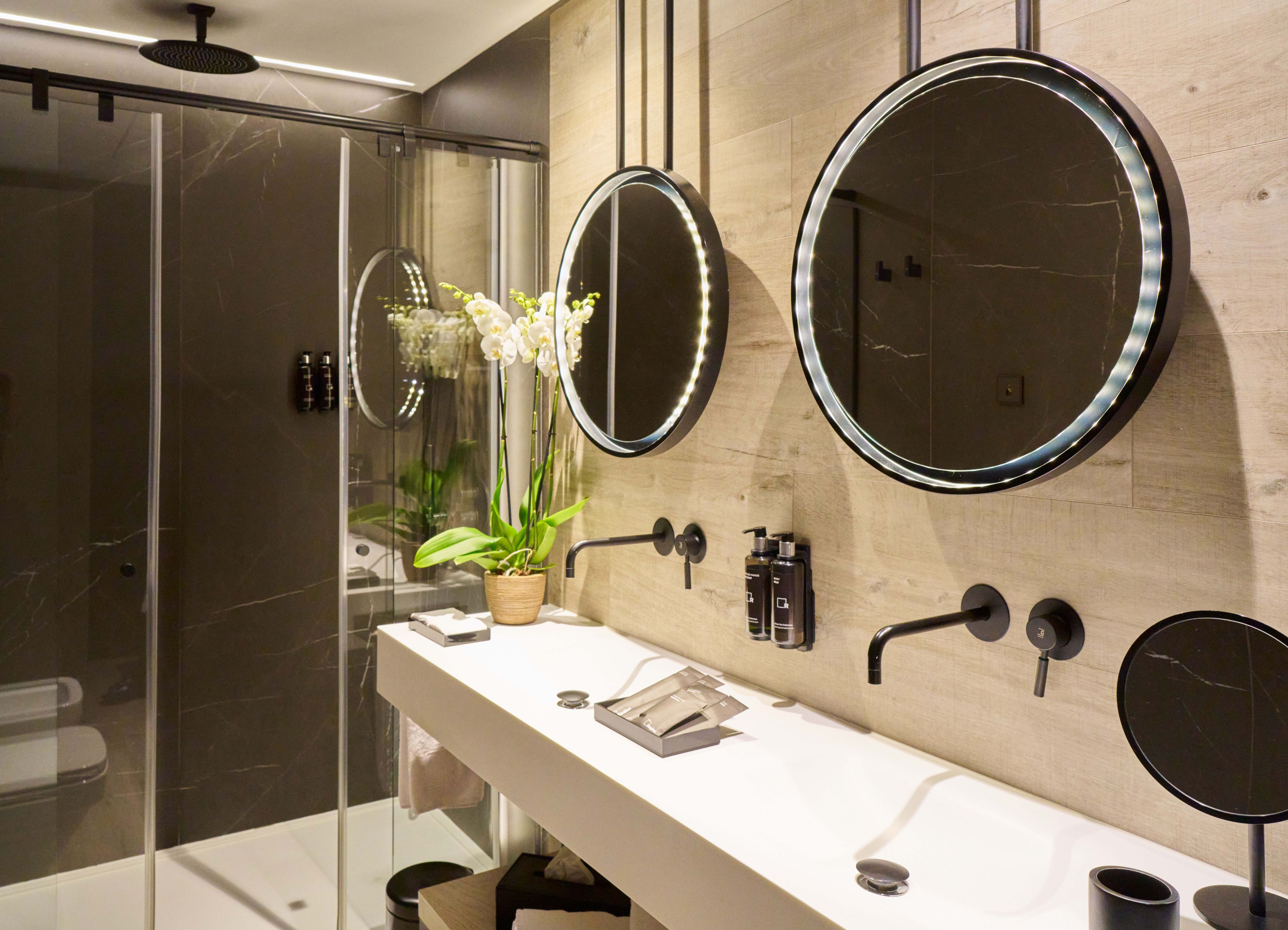 A modern bathroom with a glass shower enclosure, a white vanity with a mirror, and a potted orchid.