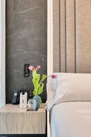 Ein Hotelzimmer mit Marmorwand, einem Nachttisch mit Telefon, einer Wasserflasche und einer Vase mit Blumen.