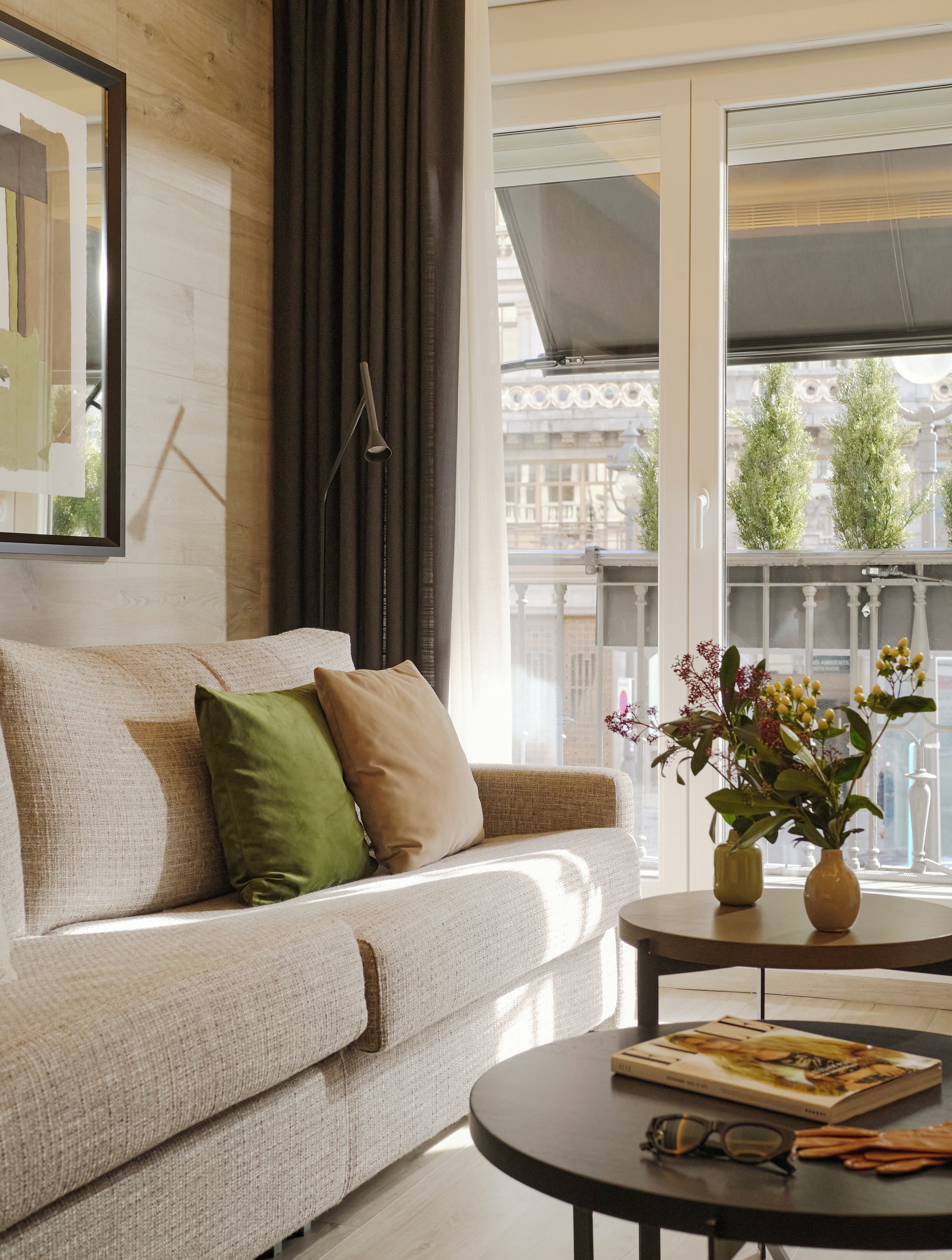 A modern living room with a sofa, a coffee table, and a window with a view of buildings and trees.