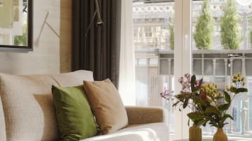 A modern living room with a sofa, a coffee table, and a window with a view of buildings and trees.