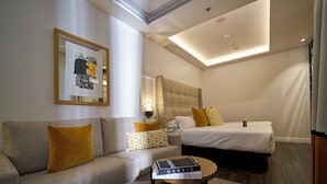 Una habitación de hotel moderna con sofá, cama, una mesita de café y una obra de arte enmarcada en la pared.