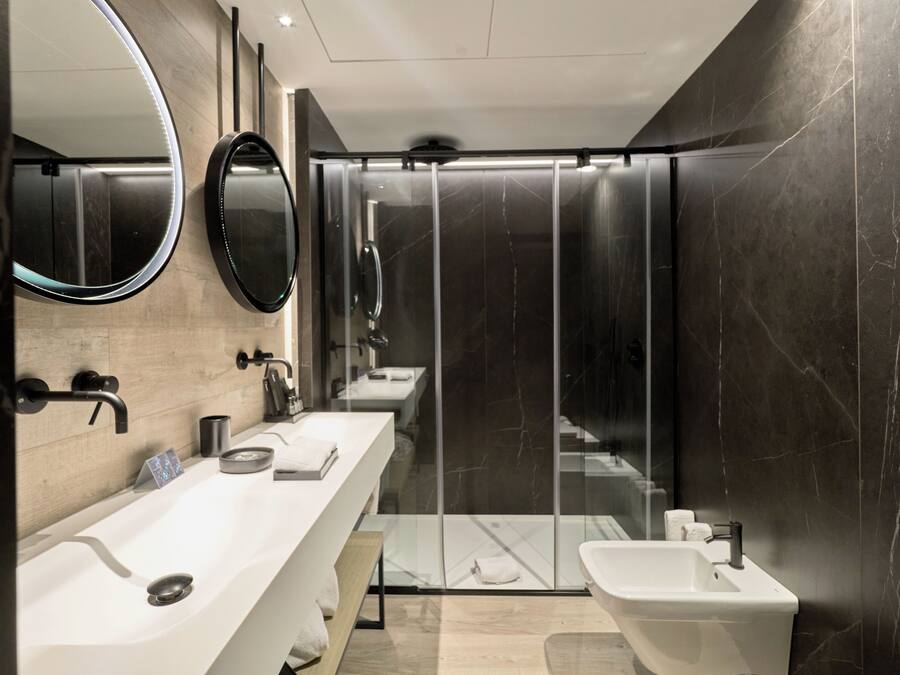 A modern bathroom with a large mirror, a vanity with a sink, a bidet, and a glass-enclosed shower.