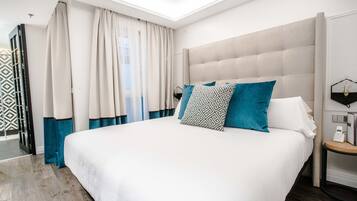 Habitación de hotel moderna con una cama grande, una mesita de noche con lámpara y vistas a la ciudad desde la ventana.