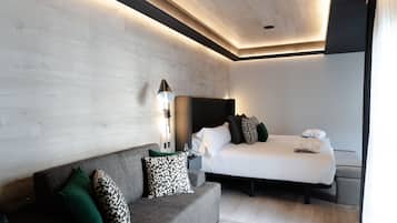 Una habitación de hotel moderna con un sofá gris, una cama con ropa blanca y una lámpara de pared.