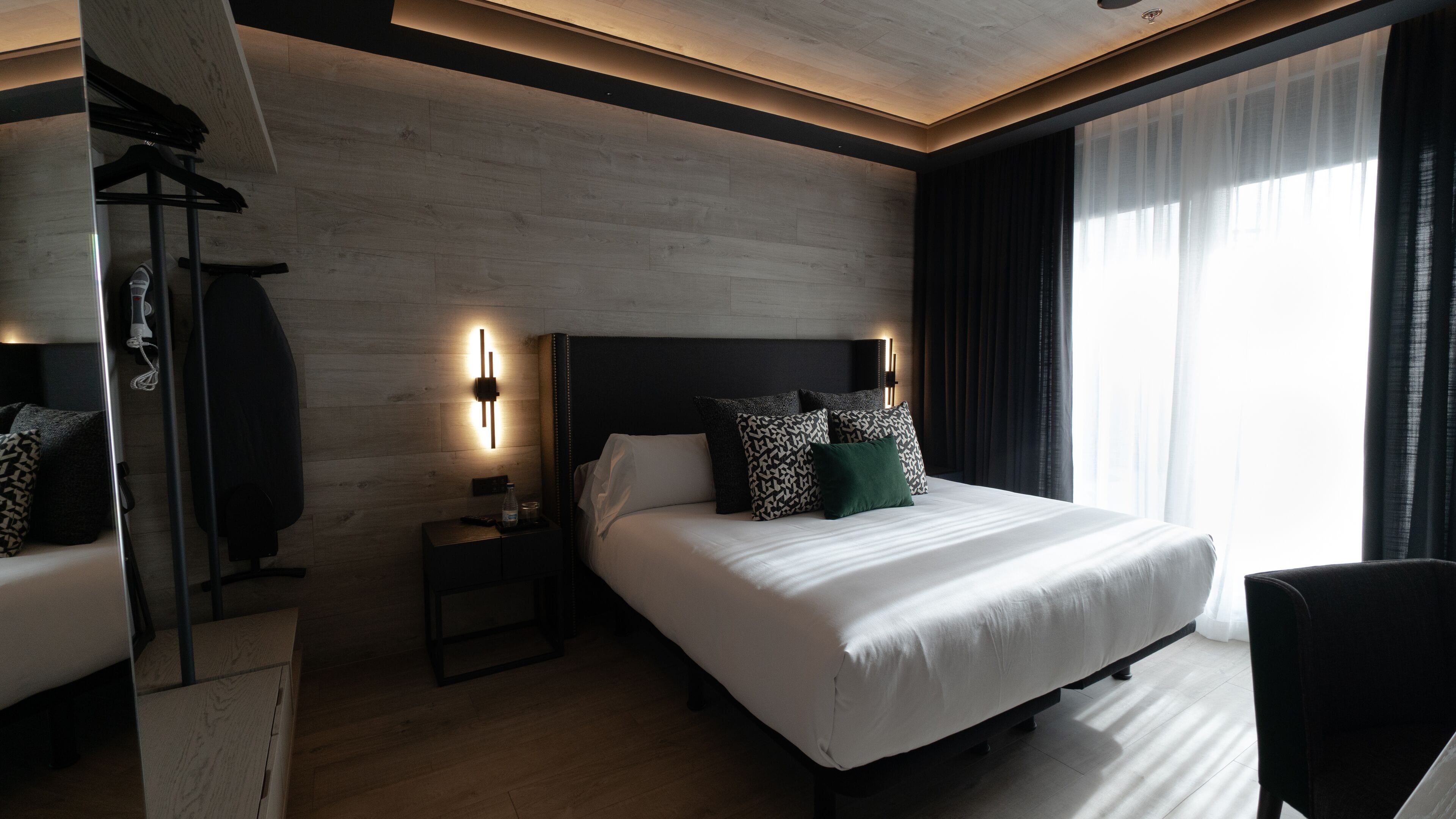 Une chambre d’hôtel moderne avec un grand lit, des tables de chevet, un miroir et une vue sur l’extérieur.